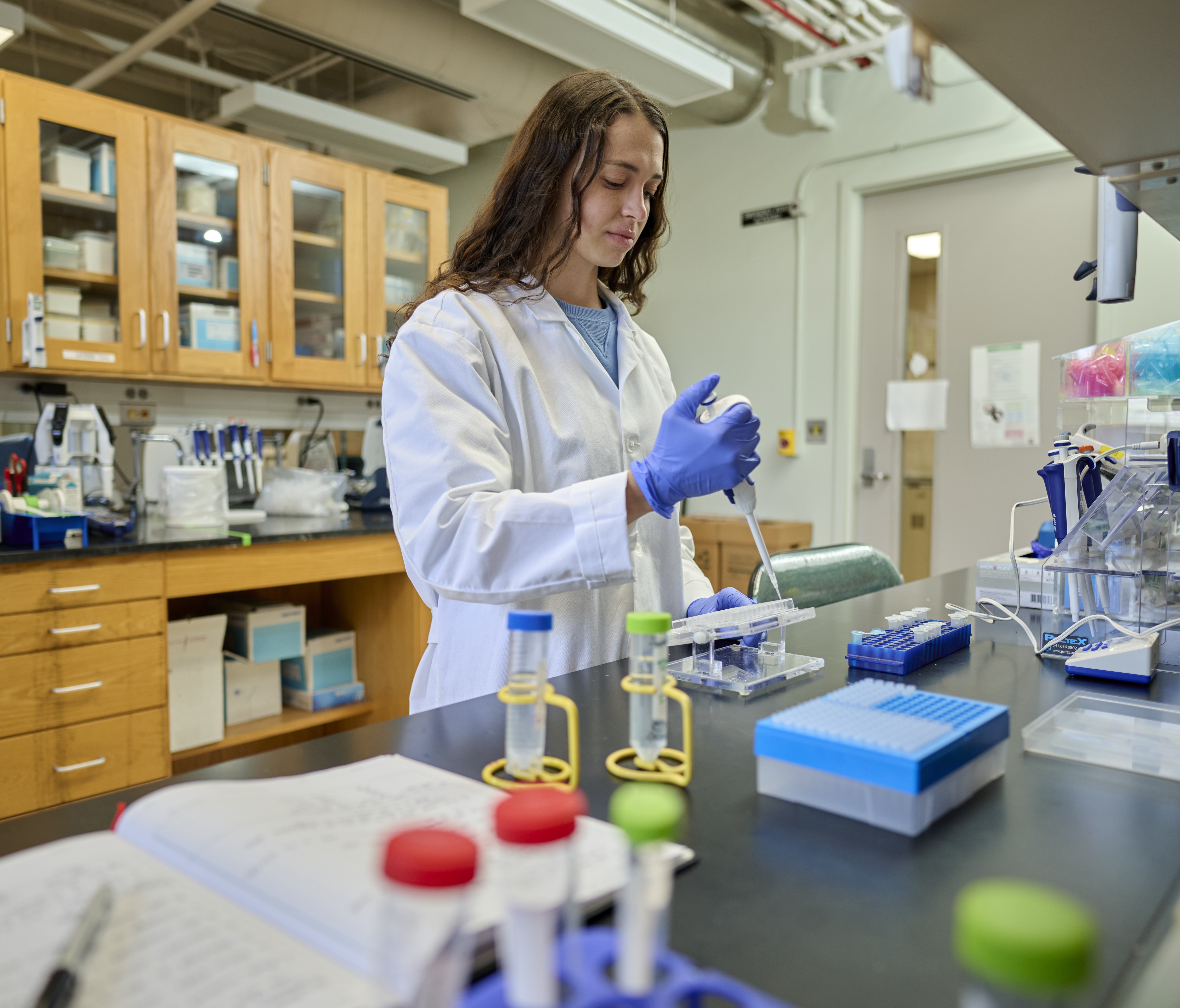 Haylee demonstrates pipetting in a laboratory setting, wearing a lab coat